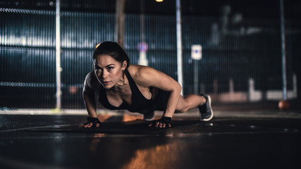 Fototapeta premium Beautiful Energetic Fitness Girl Doing Push Up Exercises. She is Doing a Workout in a Fenced Outdoor Basketball Court. Evening After Rain in a Residential Neighborhood Area.