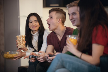 Company of young friends spending time together playing games and eating food. Young man opens his mouth waiting for his girlfriend to feed him