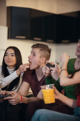 Company of young friends spending time together playing games and eating food. Young man opens his mouth and his girlfriend feed him
