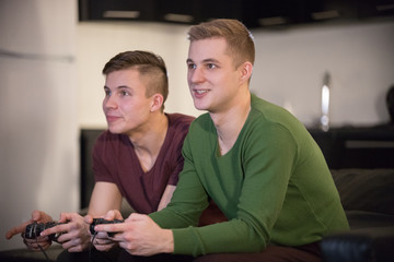 Two young men playing games at the evening holding a joysticks