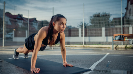 Beautiful Energetic Fitness Girl Doing Push Up Exercises. She is Doing a Workout in a Fenced Outdoor Basketball Court. Daytime After Rain in a Residential Neighborhood Area.