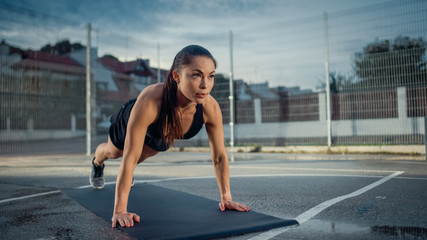 Beautiful Energetic Fitness Girl Doing Push Up Exercises. She is Doing a Workout in a Fenced Outdoor Basketball Court. Daytime After Rain in a Residential Neighborhood Area.