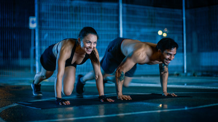 Fototapeta premium Smiling Happy Athletic Fitness Couple Doing Mountain Climber Exercises. Workout is Done in a Fenced Outdoor Basketball Court. Night After Rain in a Residential Neighborhood Area.
