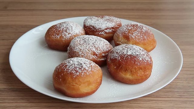 Homemade donuts sprinkled with powdered sugar on a round white plate. A man takes a donut from a plate.