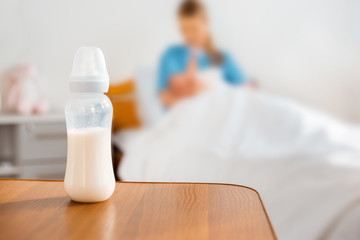 close-up view of baby bottle with milk and mother breastfeeding newborn baby in hospital room