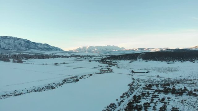 Aerial descending over snowy fields in shade of the setting sun with sunlit mountain in the far distance