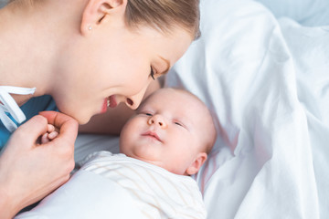 happy young mother holding hand of adorable newborn baby lying on bed
