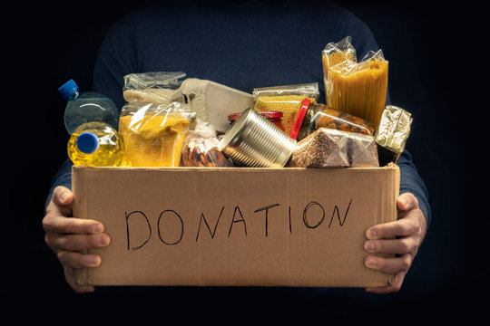 A man holding a donation box of different products on dark background