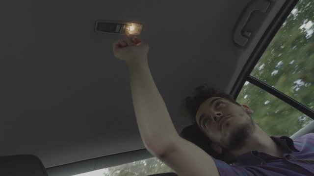 Bored teen man playing during road trip turning on and turning out the light of the car roof