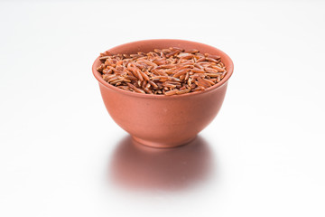 Brown rice in a clay cup on a white background