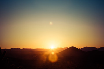 Obraz premium Słońce wschodzące nad pustynią w Arizonie z czterema szczytami w odległym tle i czystym błękitnym niebem.