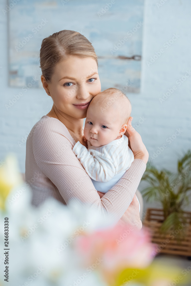 Wall mural selective focus of happy young mother hugging infant baby and smiling at camera