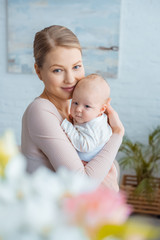selective focus of happy young mother hugging infant baby and smiling at camera