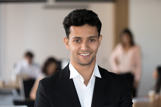 Young Smiling Arabic Businessman In Suit Looking At Camera In Office With Team At Background, Successful Manager, Arab Millennial Corporate Employee Leader, Happy Coach Executive Head Shot Portrait