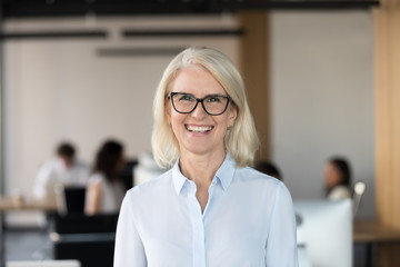 Cheerful senior businesswoman in glasses looking at camera, happy older team leader ceo manager, female aged teacher professor or mature executive woman mentor smiling in office head shot portrait