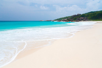 White sand beach with waves and hills with green plants