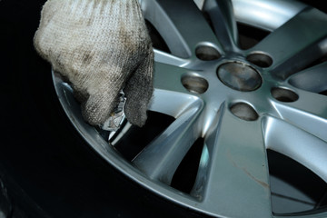 the hand of repair man and dirty white glove refueling air into the tyre of the metallic iron wheel