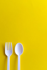 Minimalistic white reusable plastic spoon fork knife cutlery isolated on yellow background laying on the table with copy space. Top view flat lay perspective. Plastic concern.