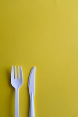 Minimalistic white reusable plastic spoon fork knife cutlery isolated on yellow background laying on the table with copy space. Top view flat lay perspective. Plastic concern.