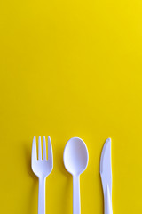 Minimalistic white reusable plastic spoon fork knife cutlery isolated on yellow background laying on the table with copy space. Top view flat lay perspective. Plastic concern.
