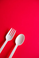 Minimalistic white reusable plastic spoon fork knife cutlery isolated on red background laying on the table with copy space. Top view flat lay perspective. Plastic concern.