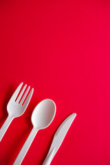 Minimalistic white reusable plastic spoon fork knife cutlery isolated on red background laying on the table with copy space. Top view flat lay perspective. Plastic concern.
