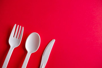 Minimalistic white reusable plastic spoon fork knife cutlery isolated on red background laying on the table with copy space. Top view flat lay perspective. Plastic concern.