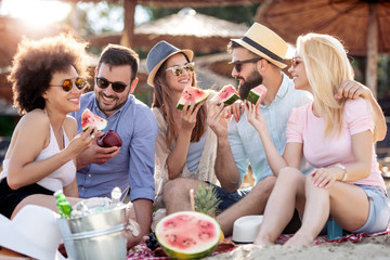 Happy young friends eating watermelon on beach