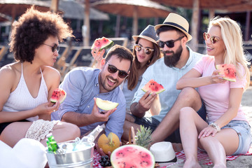 Happy young friends eating watermelon on beach