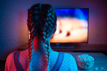 A young girl watching movies with a bowl of popcorn on the background of the TV. A bright color of...