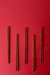 Modern Chinese wooden chopsticks repeat pattern isolated on colorful red background with small dried flowers with copy space. Top view flat lay perspective.