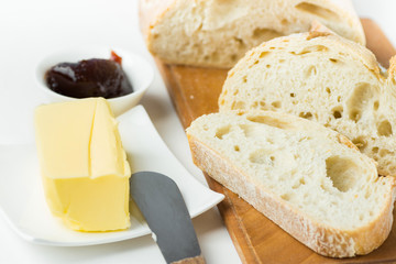 Breakfast table setting. Freshly baked artisan sliced bread on wood cutting board stick of organic butter homemade strawberry marmalade knife on white kitchen table. Morning energy cozy home