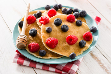 Pancakes with raspberries, blueberries and honey on white wooden table