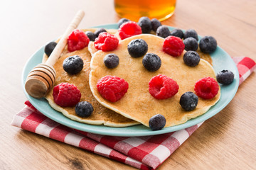 Pancakes with raspberries, blueberries and honey on wooden table