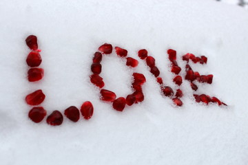 Word Love made of pomegranate seeds on white snow. Valentine's Day concept. Selective focus.