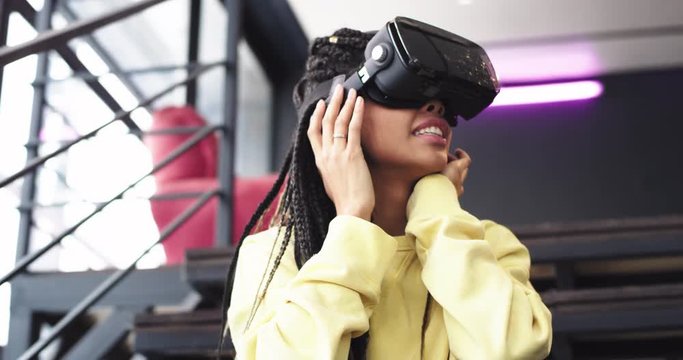 Portrait impressed african lady using a virtual reality glasses to travel around the world, she are very excited, sitting down on the stairs in a modern office building
