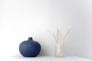 Blue round ceramic China vase and glass vase with wicker rattan reed on white table top on white background in natural light with copy space Minimal Asian interior styling.