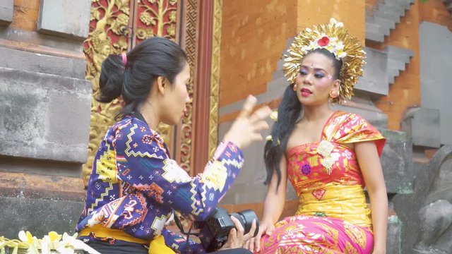 Beautiful balinese woman talking with a reporter or photographer while wearing traditional clothes and sitting in the temple. Shot in 4k resolution