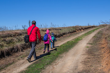 Father with children is walking along the path in boots and with backpacks.