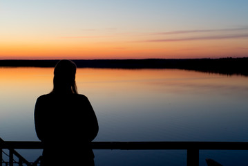 Fototapeta premium Young woman at sunset near lake silhouette