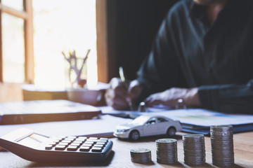 Car insurance and car service. Businessman with stack of coins and toy car, business and financial concept.