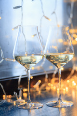 Closeup of two glasses of white wine in transparent crystal glasses on background of window and garlands. Concept romantic dinner in Michelin premium restaurant, party, February 14, March 8