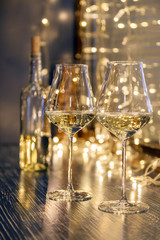Closeup of two glasses of white wine in transparent crystal glasses on background of window and garlands. Concept romantic dinner in Michelin premium restaurant, party, February 14, March 8