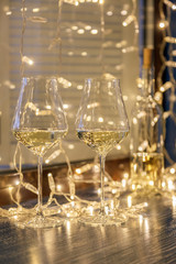 Closeup of two glasses of white wine in transparent crystal glasses on background of window and garlands. Concept romantic dinner in Michelin premium restaurant, party, February 14, March 8