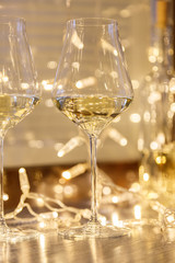 Closeup of two glasses of white wine in transparent crystal glasses on background of window and garlands. Concept romantic dinner in Michelin premium restaurant, party, February 14, March 8