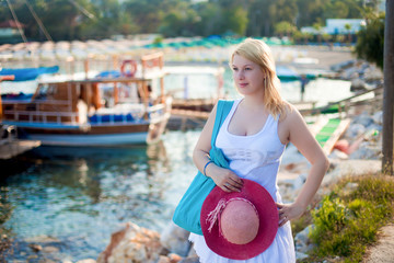 Young sexy blonde woman in white dress near sea nad yachts in marina