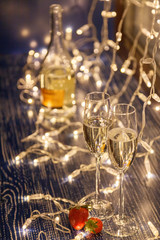 Closeup fresh strawberries, two crystal glasses, bottle of champagne sparkling wine on background of window, garlands, bokeh. Concept cozy evening in michelin restaurant, dating, dinner, Valentine Day