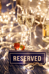 Closeup strawberry, two crystal glasses, bottle champagne sparkling wine, reserved nameplate wooden table, window, garlands. Concept date evening in restaraunt, 8 march, Valentine's Day, christmas