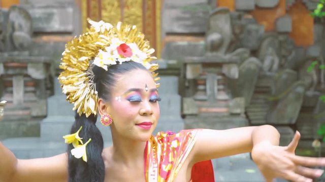 Attractive female balinese dancer dancing in the temple while wearing traditional clothes and smiling at the camera. Shot in 4k resolution