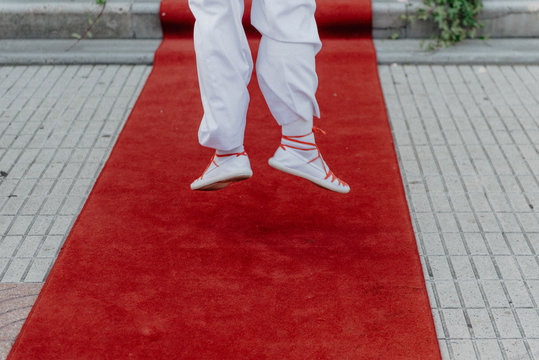 Person in white cloth and gym shoes jumping on red carpet